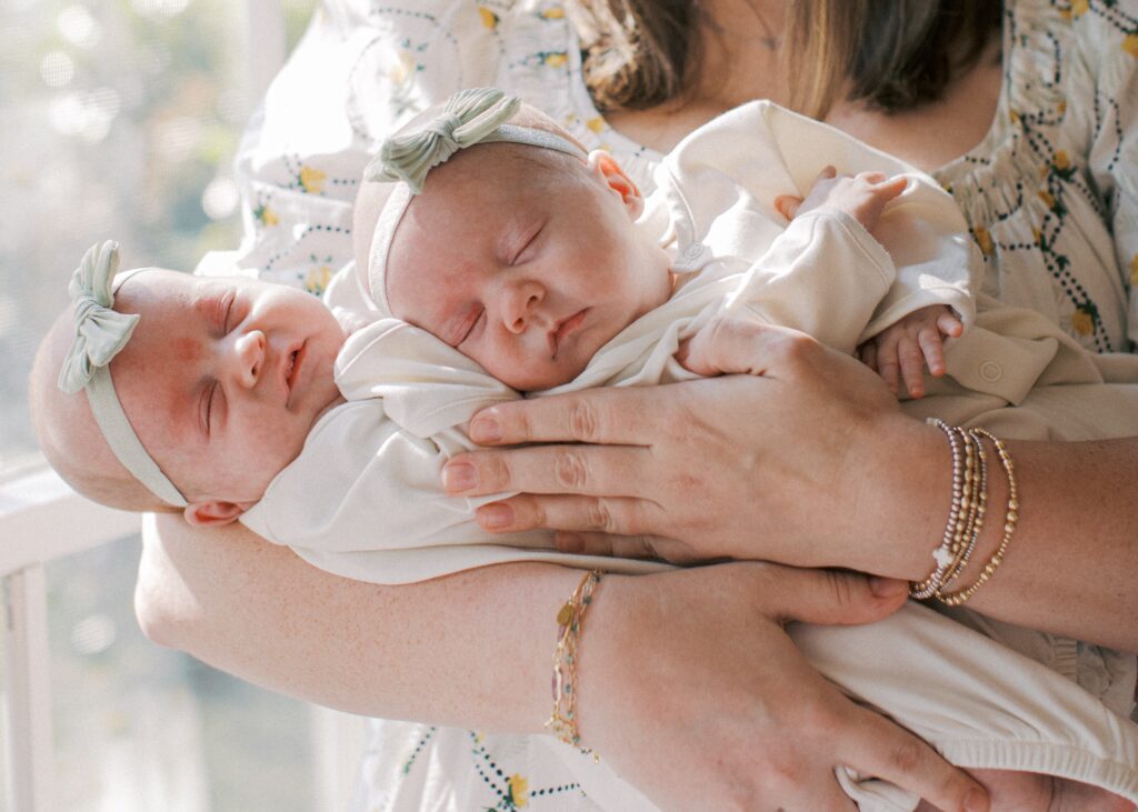 mom holding newborn twins next to a window